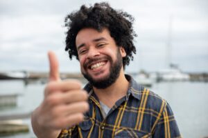 Happy man with a thumbs up gesture by the marina, expressing satisfaction and positivity.